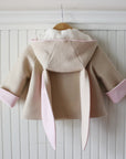 Tan bunny coat hung up showing pink, rolled sleeve cuffs, pink lining of ears, and white lining of the hood.