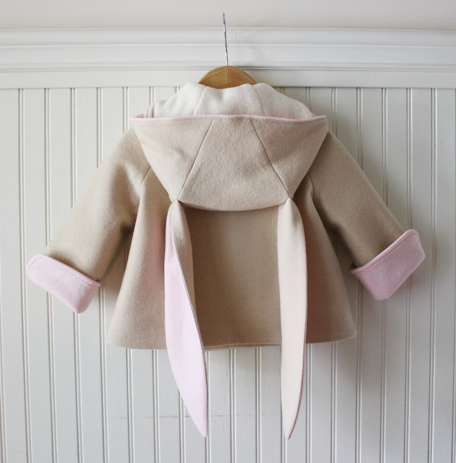 Tan bunny coat hung up showing pink, rolled sleeve cuffs, pink lining of ears, and white lining of the hood.