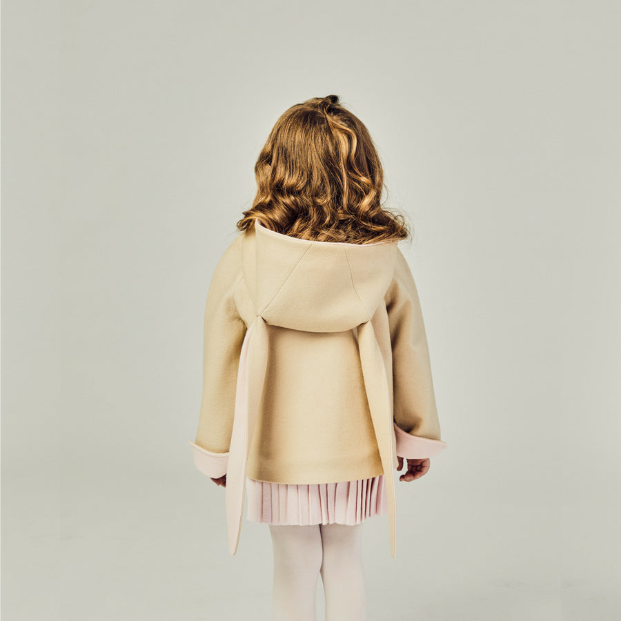 Back view of the tan bunny coat on the model, displaying floppy bunny ears with the hood down.