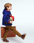 Boy wearing Paddington Blue duffle coat with toggles carrying Paddington Bear plush toy gift set