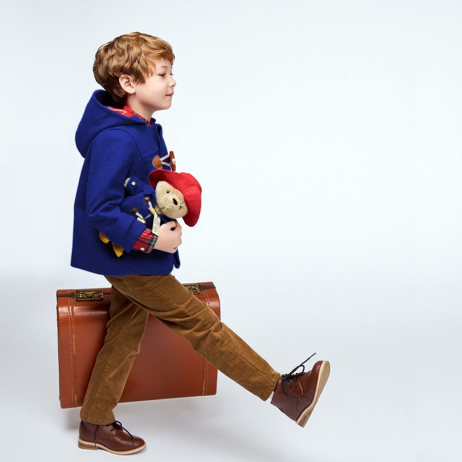 Boy wearing Paddington Blue duffle coat with toggles carrying Paddington Bear plush toy gift set
