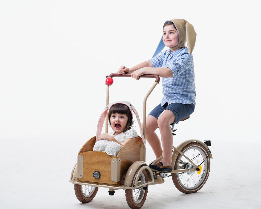 Boy and girl model wearing tan and oatmeal bunny hats while riding in bikewagon.