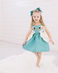 Little Goodall Girl model wearing blue dress with two swans on either side of the dress.