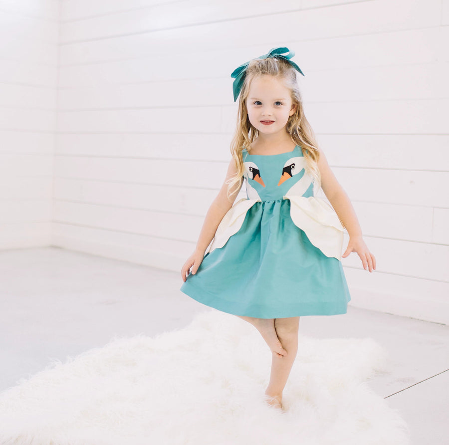 Little Goodall Girl model wearing blue dress with two swans on either side of the dress.