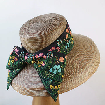 Wide-brim natural palm hat with floral embroidered bow on black band, shown from back view