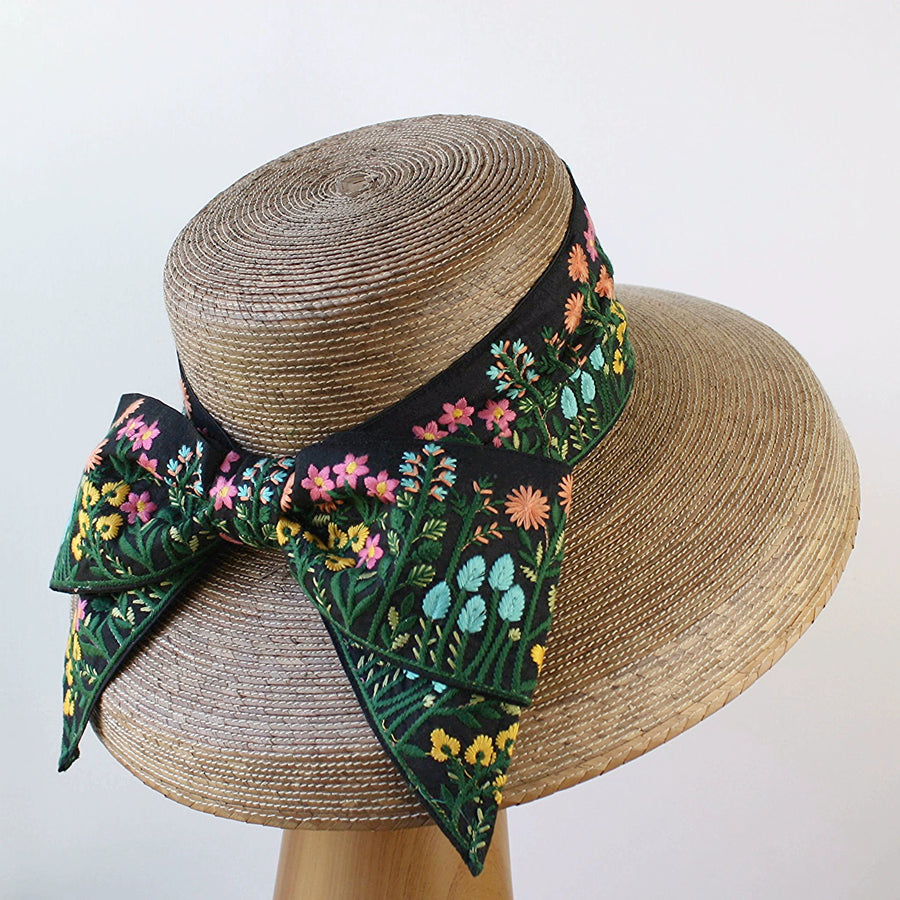 Wide-brim natural palm hat with floral embroidered bow on black band, shown from back view