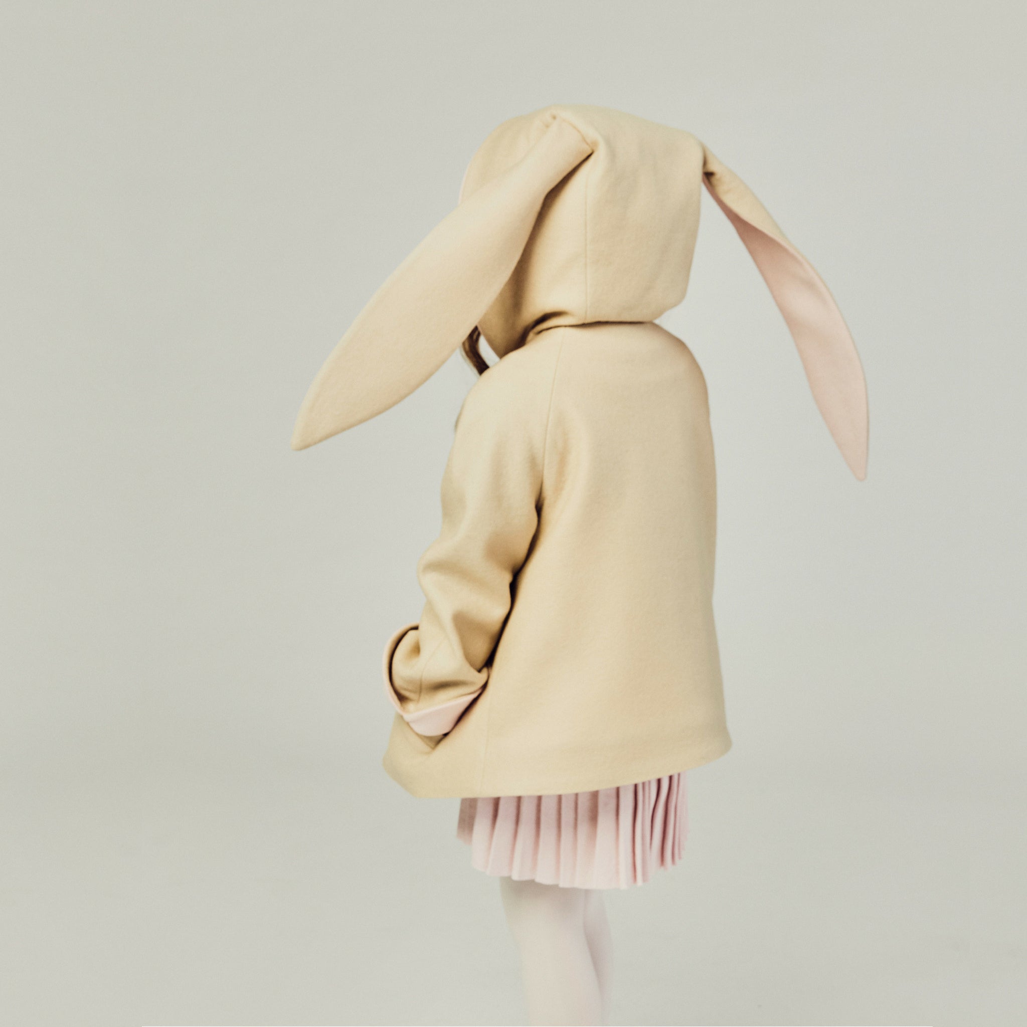 Back view of the tan bunny coat on the model, displaying floppy bunny ears with the hood up.