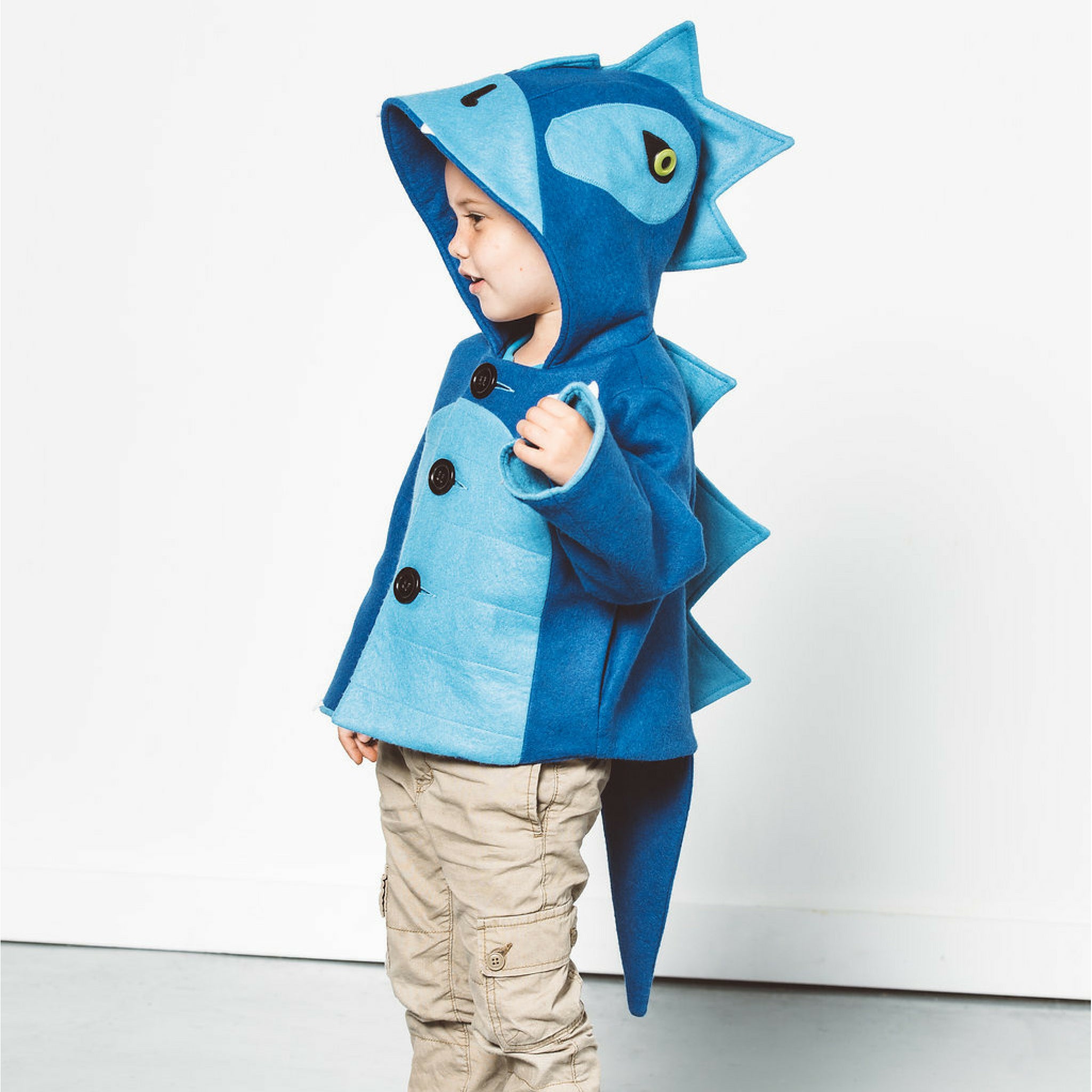 kid the Blithe Blue Dinosaur Coat by Little Goodall, a cozy wool blend jacket with a hood, ridged back, and playful tail.