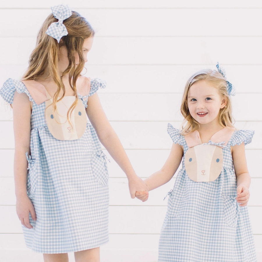 Two young girls wearing blue gingham bunny dresses by Little Goodall, each with matching blue gingham hair bows