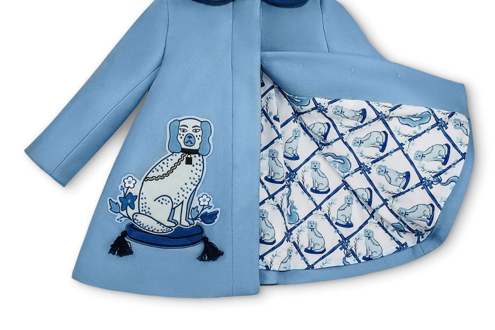 Close-up of girls' blue wool coat featuring embroidered dog motif with tassels and satin lattice print lining with dog illustrations.