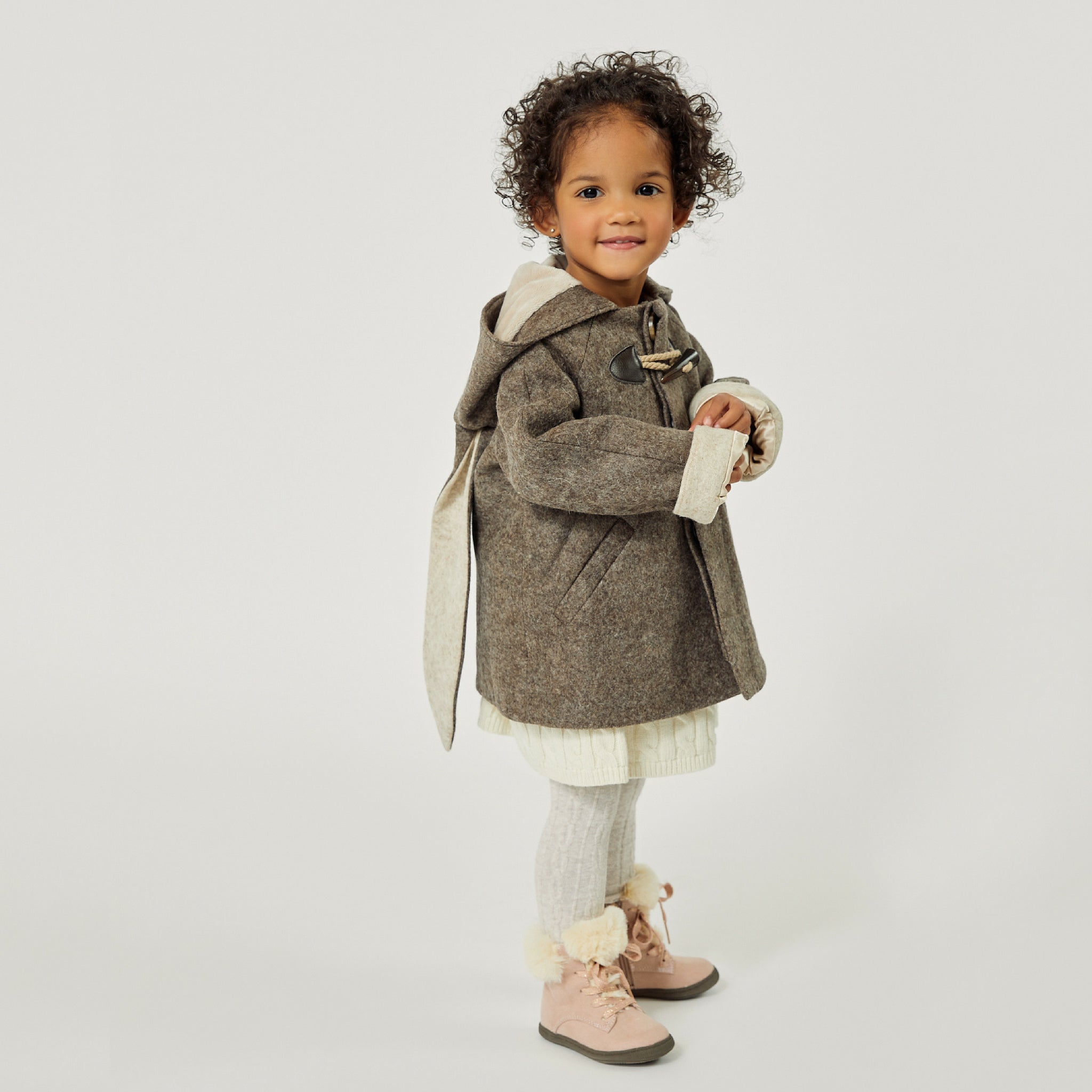 Toddler girl in little Goodall brown wool bunny coat with floppy ears, toggle closures, and a hood, standing in profile