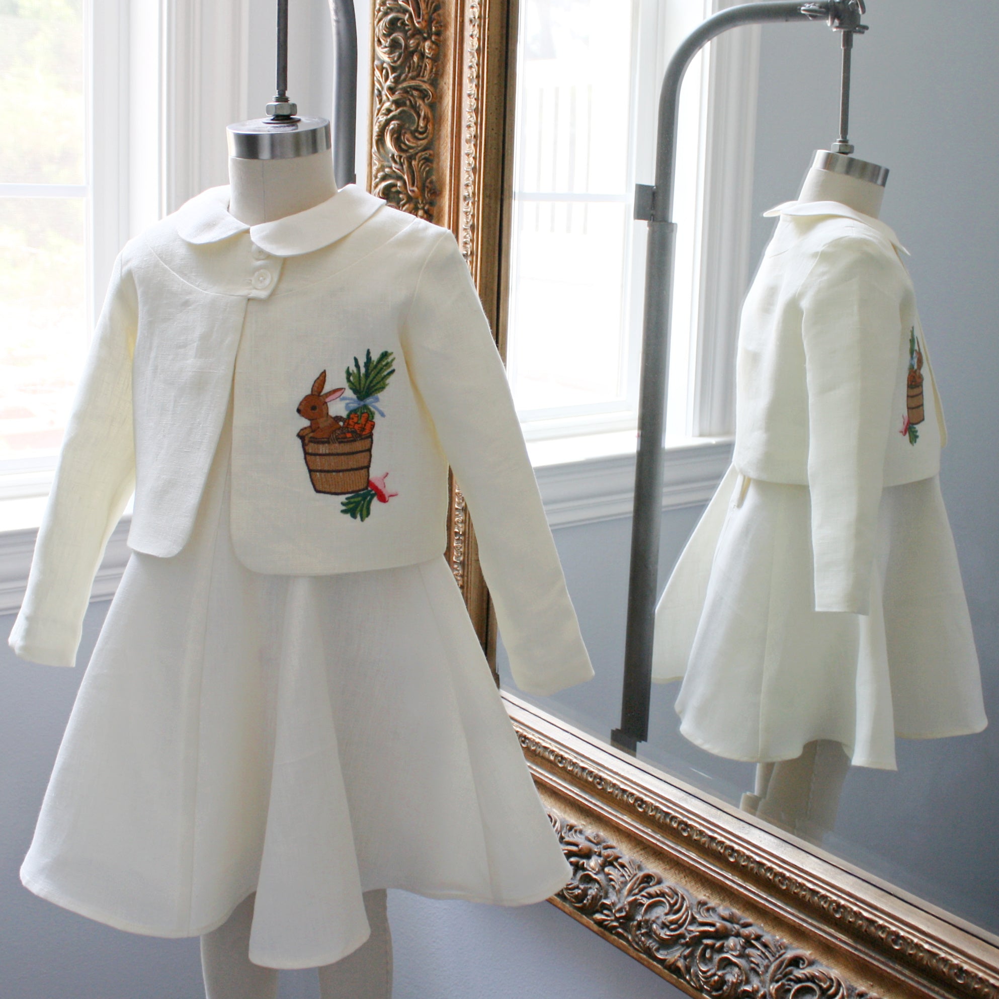 Ivory linen bunny jacket and dress set by Little Goodall displayed on a mannequin, reflected in an ornate mirror
