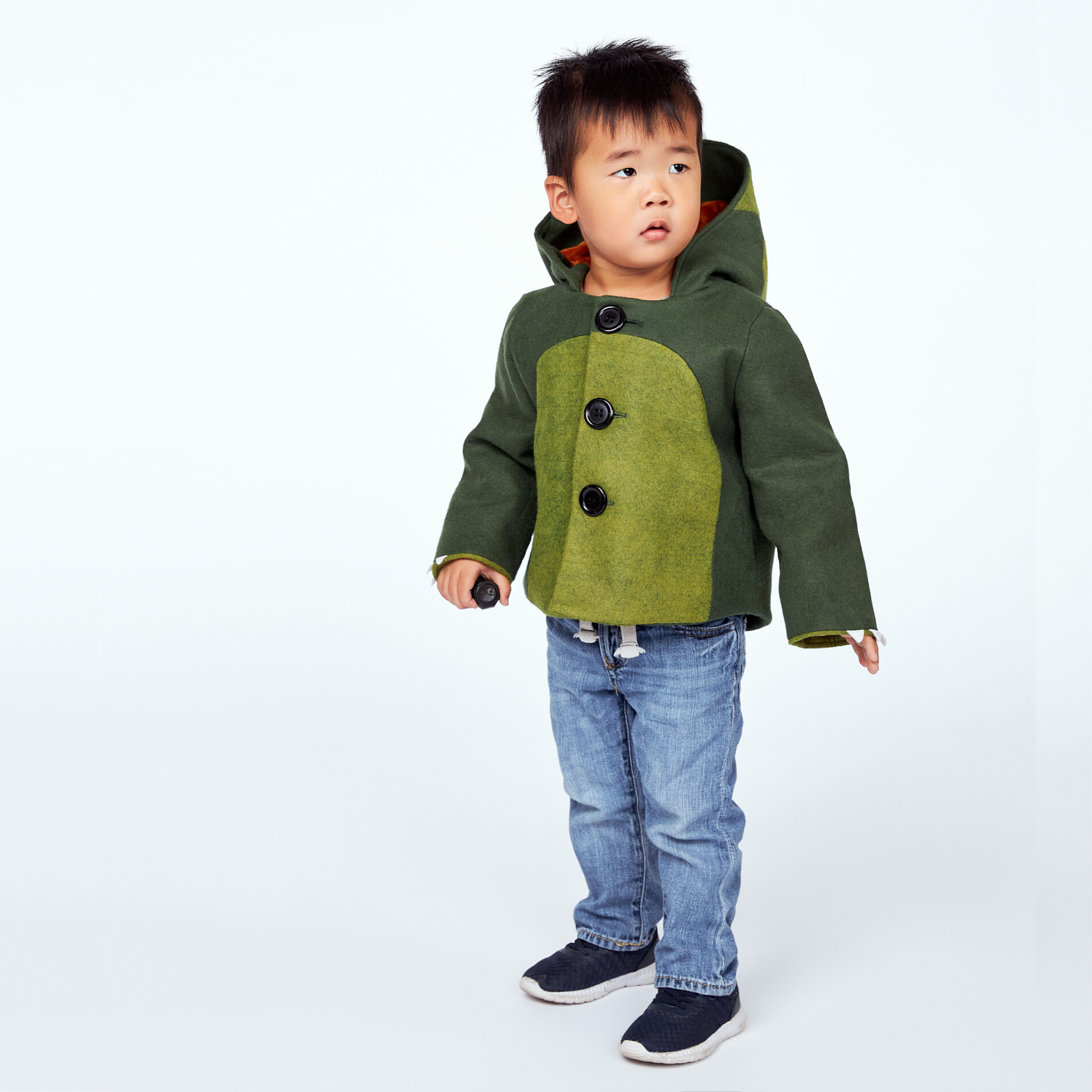 boy wearing the Little Goodall Cheeky Green Dinosaur Coat, a wool-felt jacket with big buttons, a soft plush lining, and a playful dino-inspired design