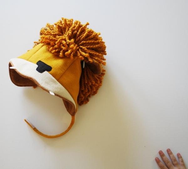 A handmade wool-blend felt lion hat with earflaps and a velcro chin strap, perfect for toddlers in cold weather.