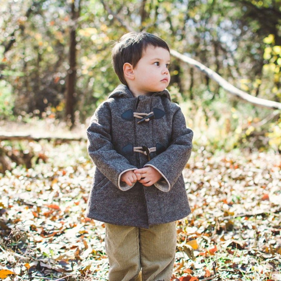 Toddler wearing the brown wool Flopsy Bunny Coat with toggle closures and a cozy hood, standing in a sunlit autumn forest