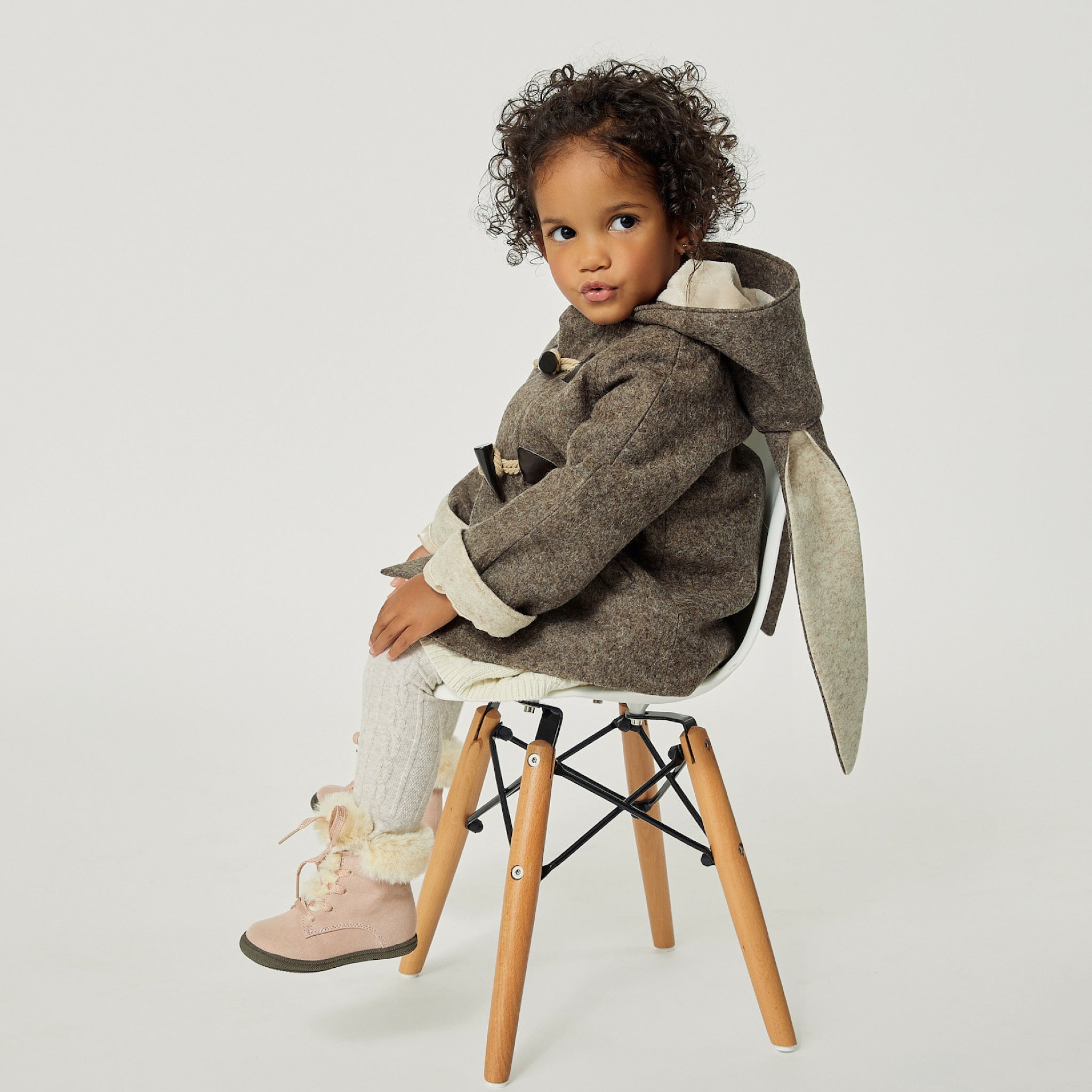 Toddler girl in a brown wool bunny coat with floppy ears, toggle closures, and a hood, sitting on a wooden chair 