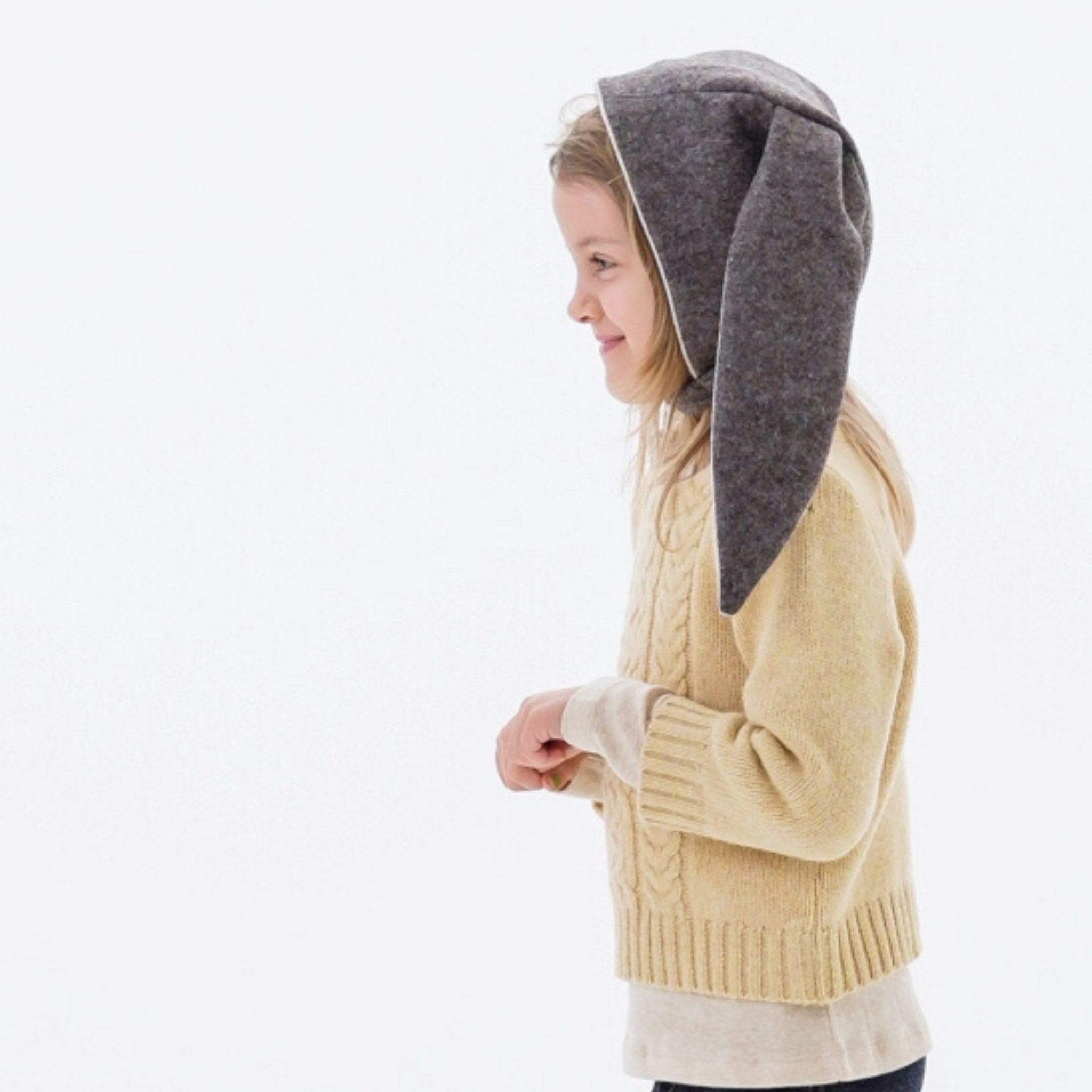 Side angle view of a child in the mushroom brown Flopsy Bunny Hat with gray floppy ears, wool felt, and a velcro chin strap