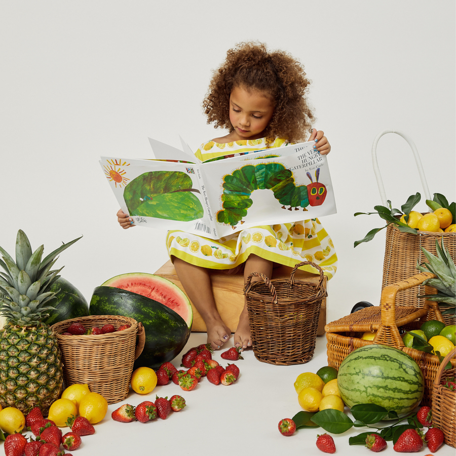 Child wearing a lemon-themed summer dress, engrossed in a Very Hungry Caterpillar  storybook