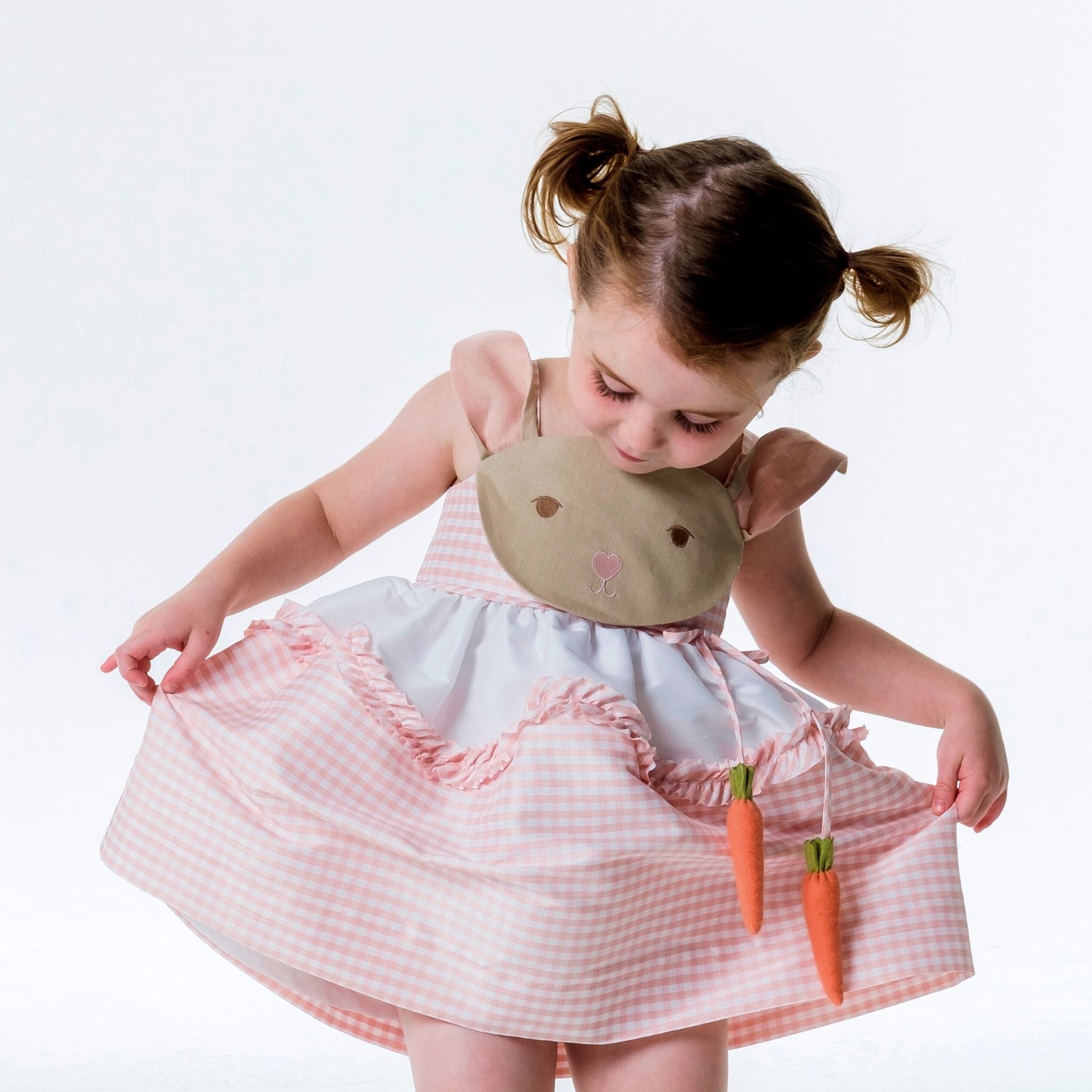 Toddler twirling in Little Goodall Pink Gingham Bunny Love Dress with embroidered bunny face, floppy ears, and dangling carrot accents.