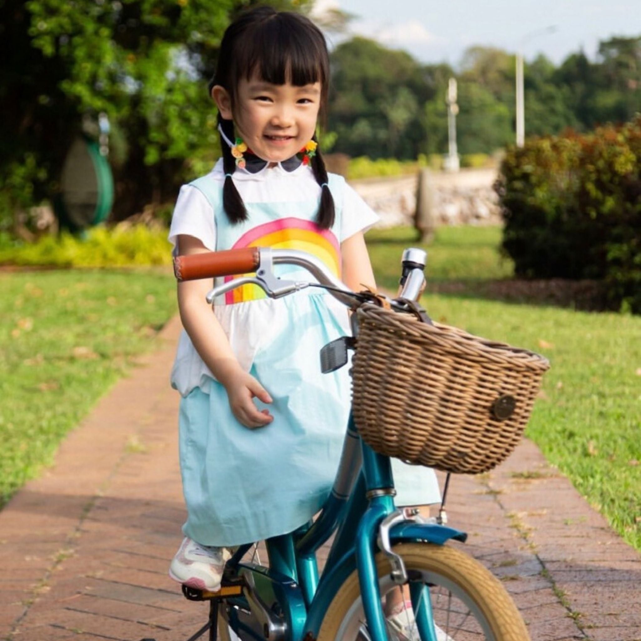 Smiling girl riding a bike in a sky blue sundress with a rainbow applique and cloud peplum