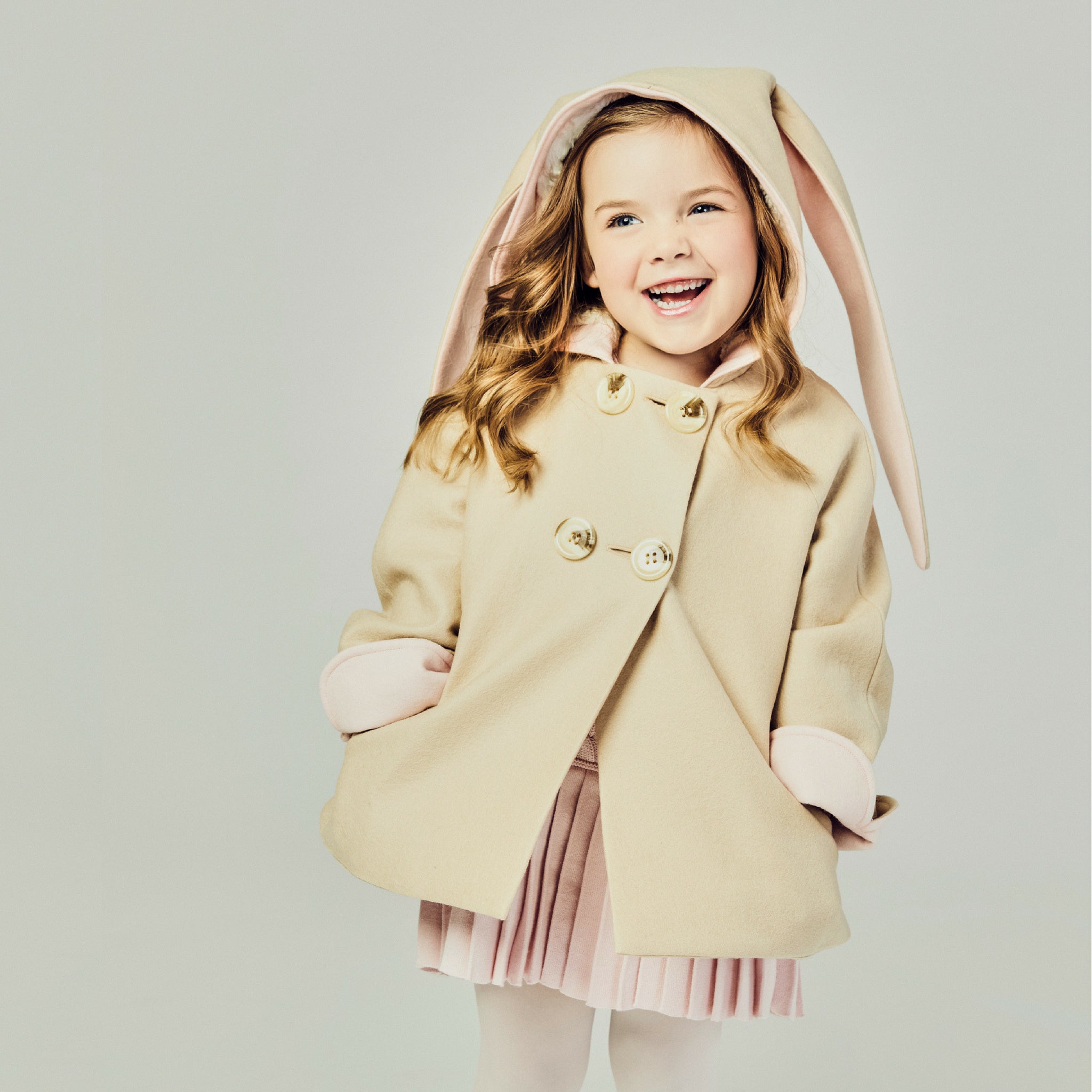 Tan bunny coat on model with her sleeve cuffs rolled up and hands in the coat pockets.