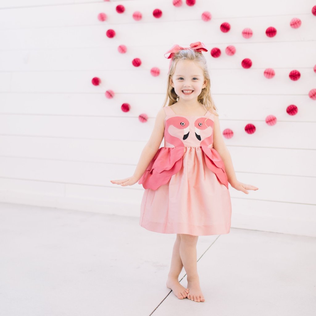 Girls in Little Goodall pink flamingo dress with sleeveless design and layered peplum, perfect for summer parties