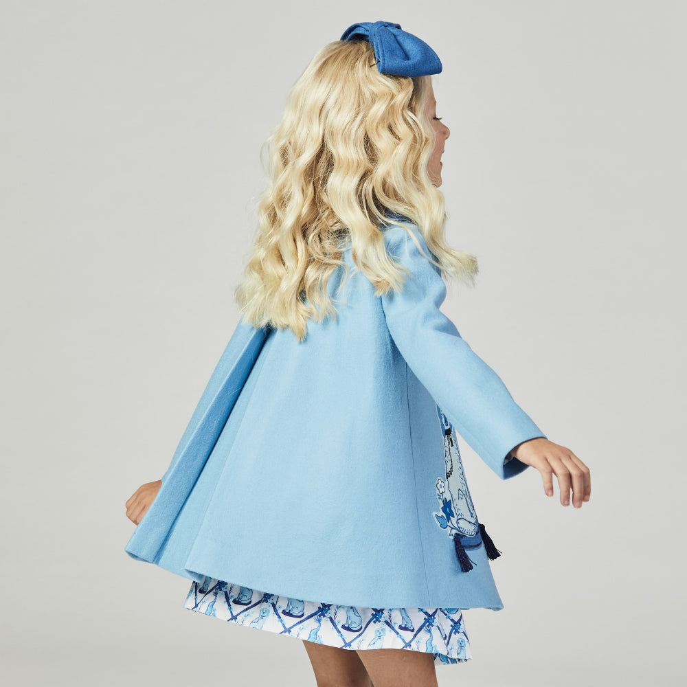 back view of girl blue wool coat with embroidered dogs, tufted pillows, and tassels, featuring Willa Heart artwork. Lined with satin lattice print