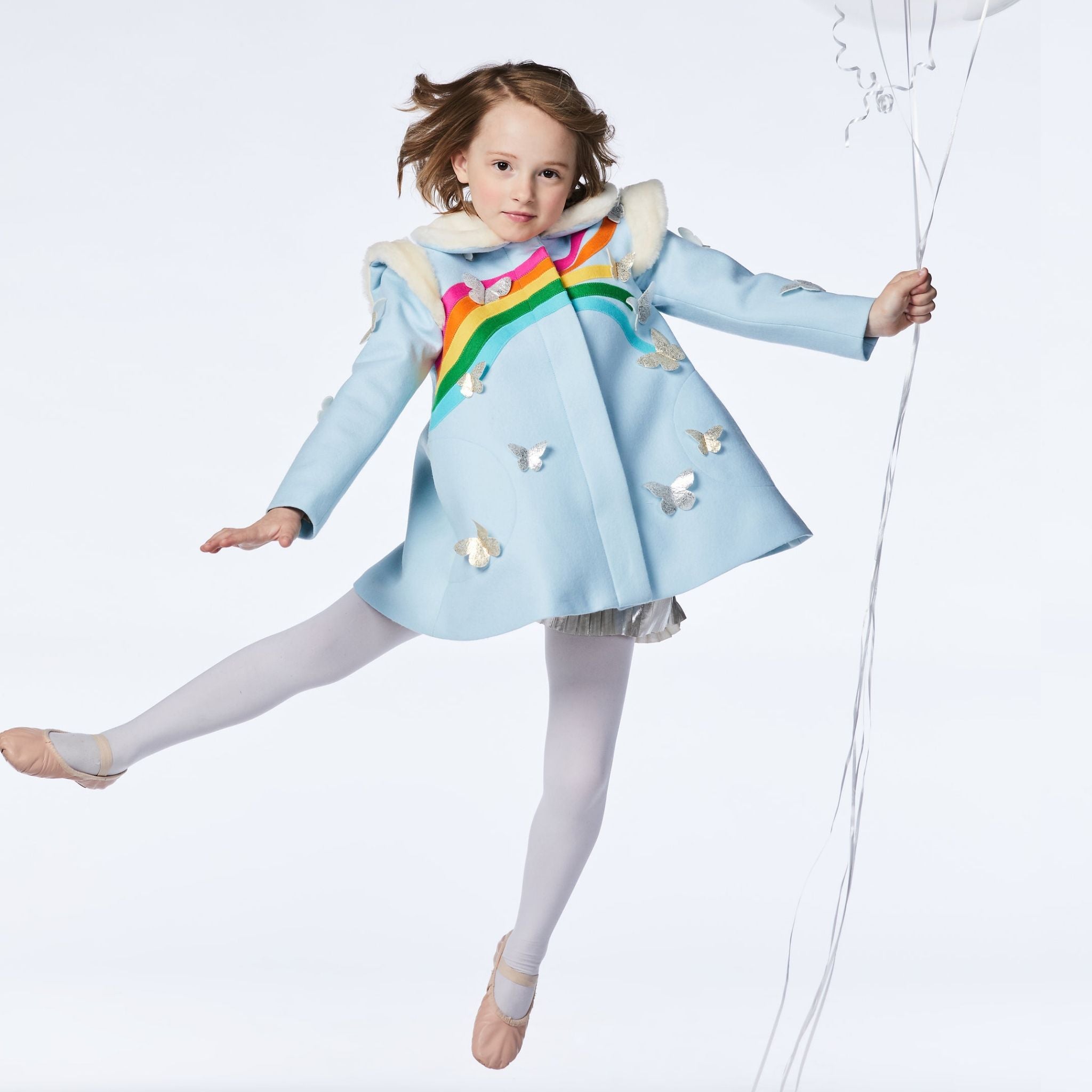 Sky blue wool coat with rainbow detail, gold and silver butterflies, and faux fur collar, worn by a girl in motion