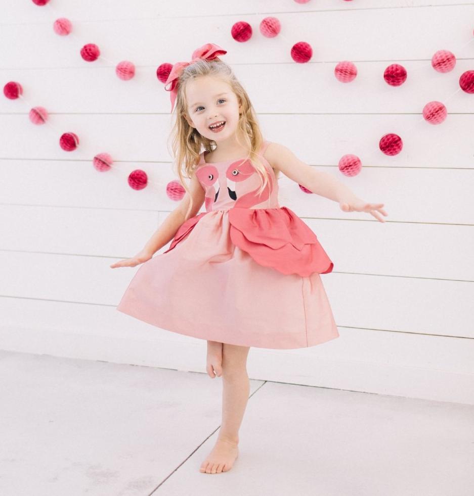 Girl smiling and twirling in Little Goodall  pink flamingo dress with layered peplum and flamingo applique