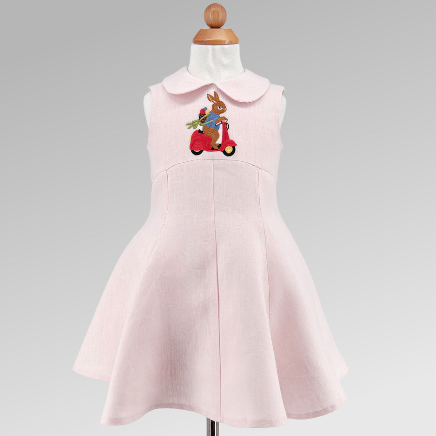 Blush Linen Scooter Bunny Dress on form, featuring embroidered bunny on red scooter, sleeveless design, and flared skirt for toddlers and girls.