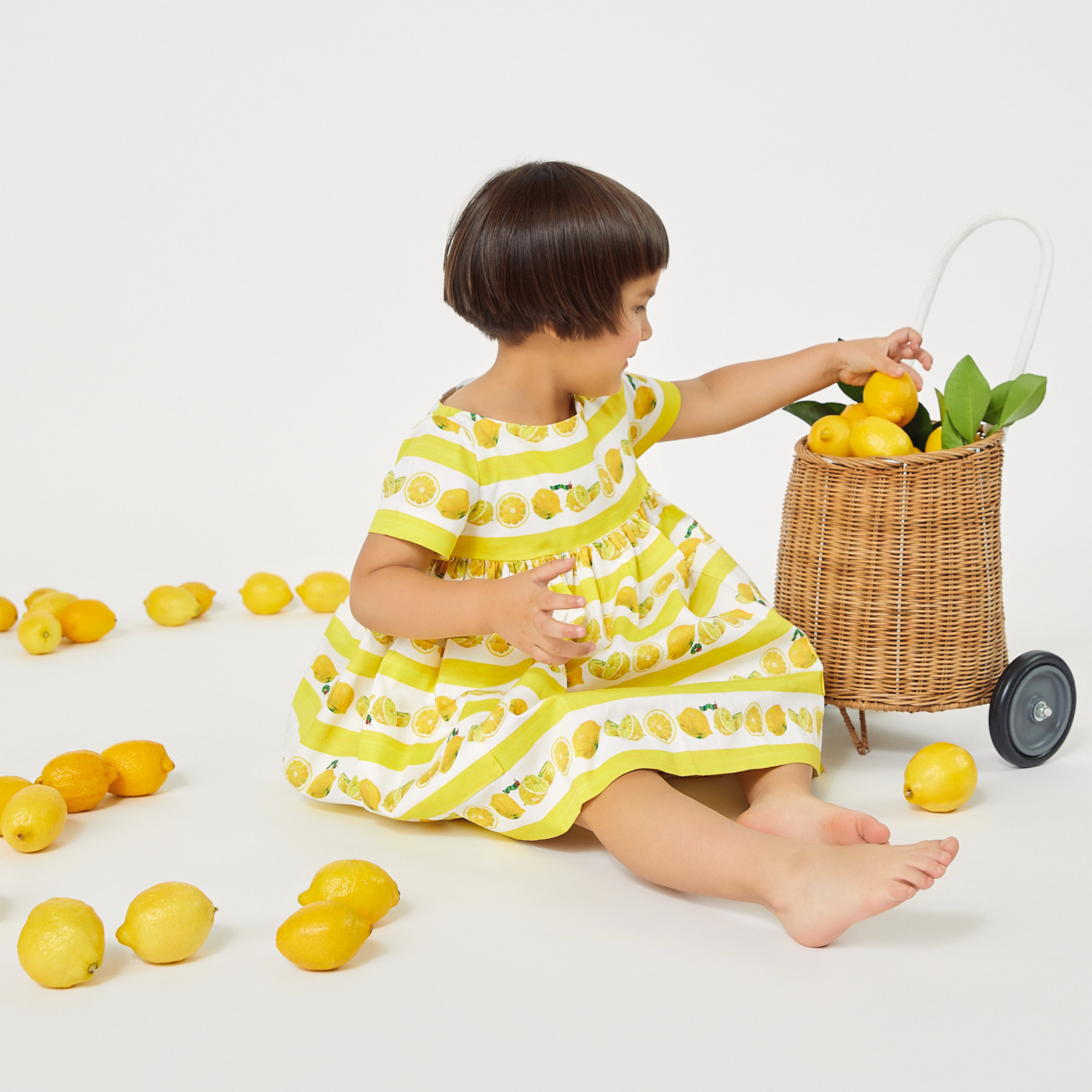 Toddler in a Very Hungry Caterpillar™ Lemonade Dress plays with fresh lemons