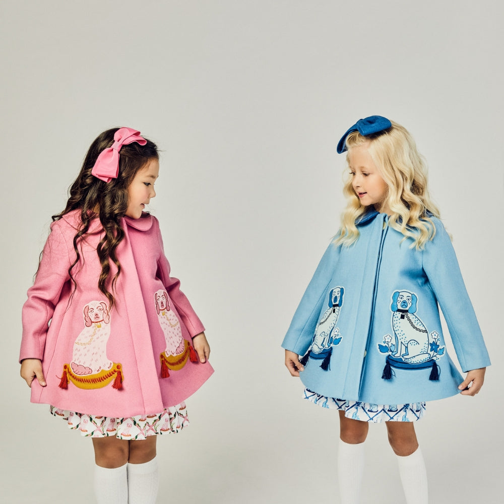 Two girls wearing blue and pink wool coats with embroidered dog designs, tassels, and coordinating bows, featuring Willa Heart artwork.
