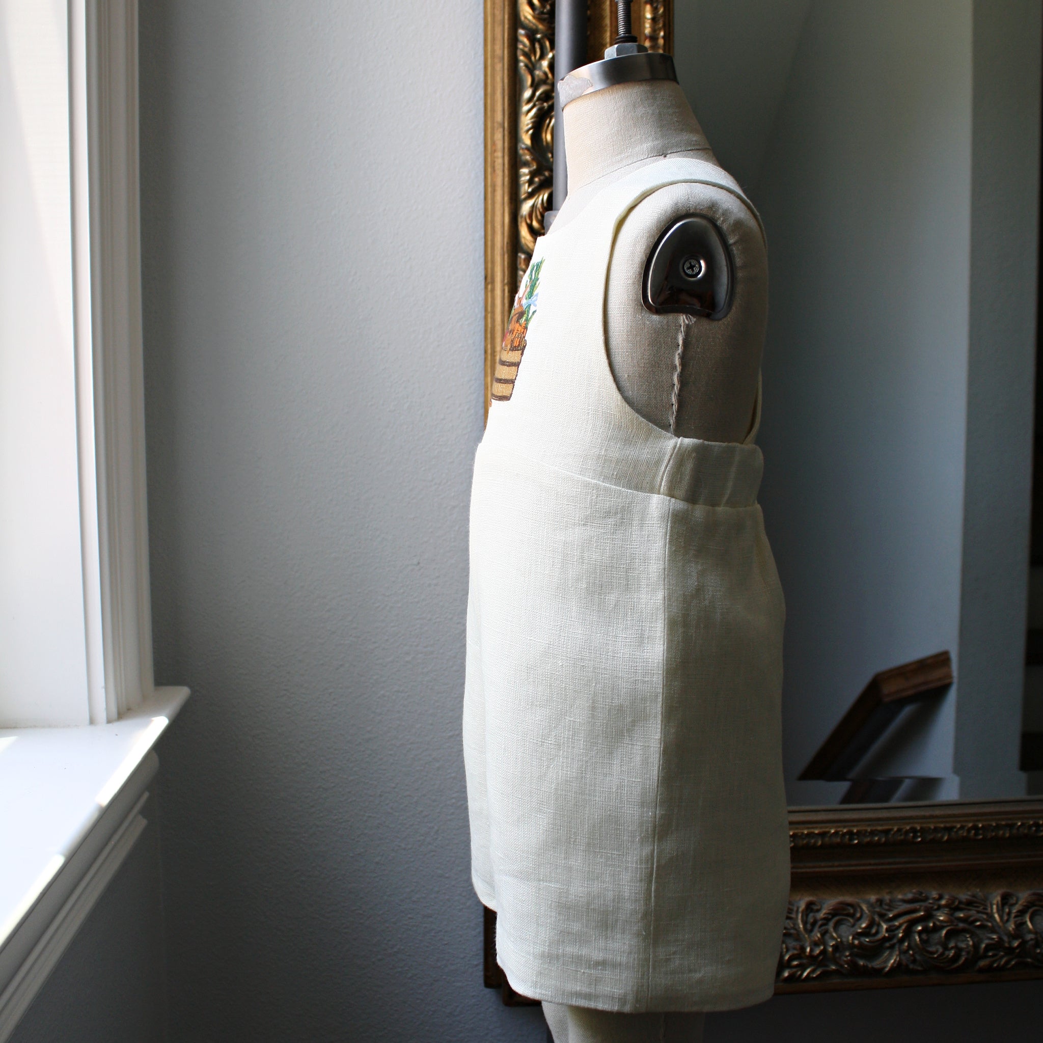 Side view of ivory linen bunny romper on a dress form, showcasing fabric texture and embroidered detail."