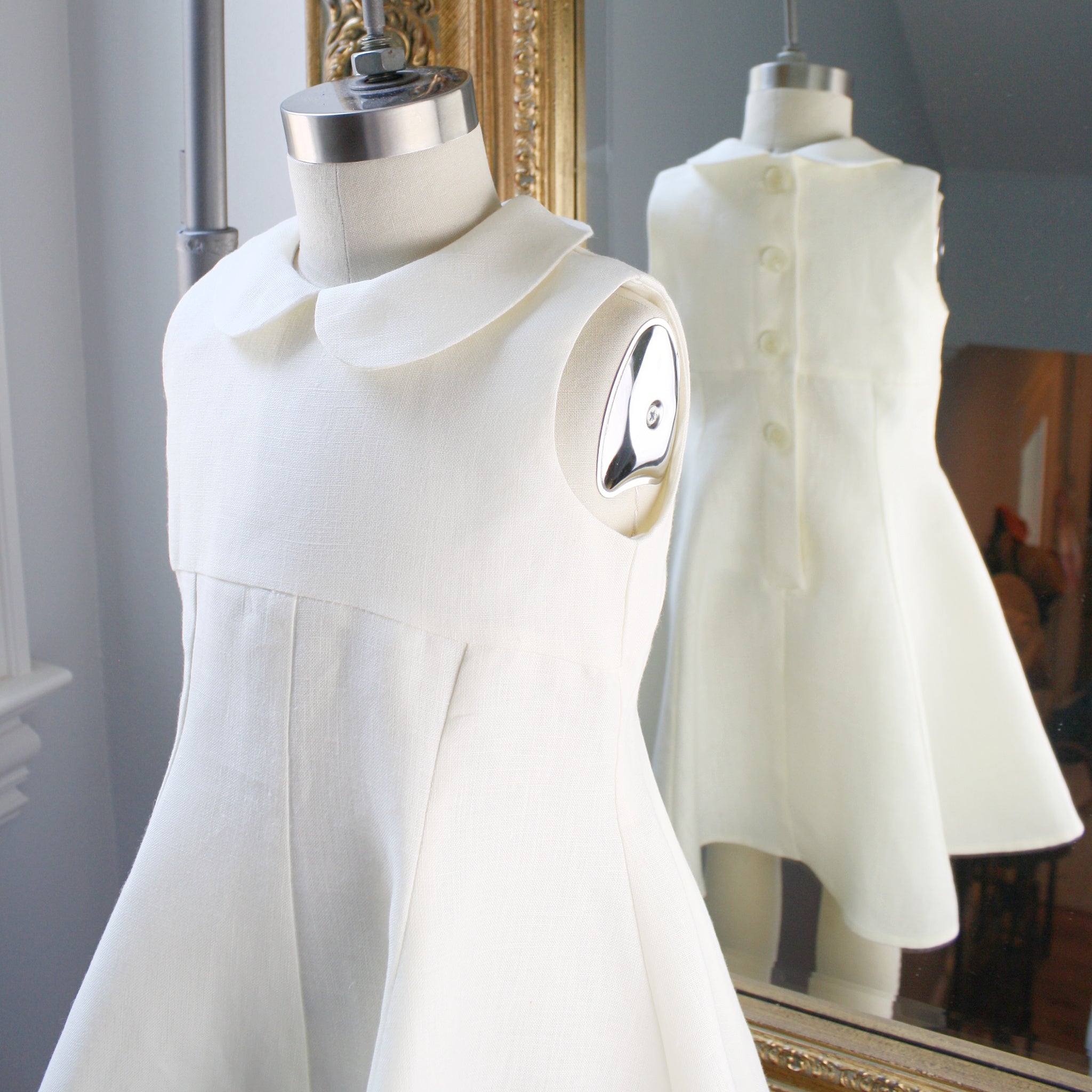 Close-up of ivory linen dress on a mannequin, showing Peter Pan collar, princess seams, and back button details