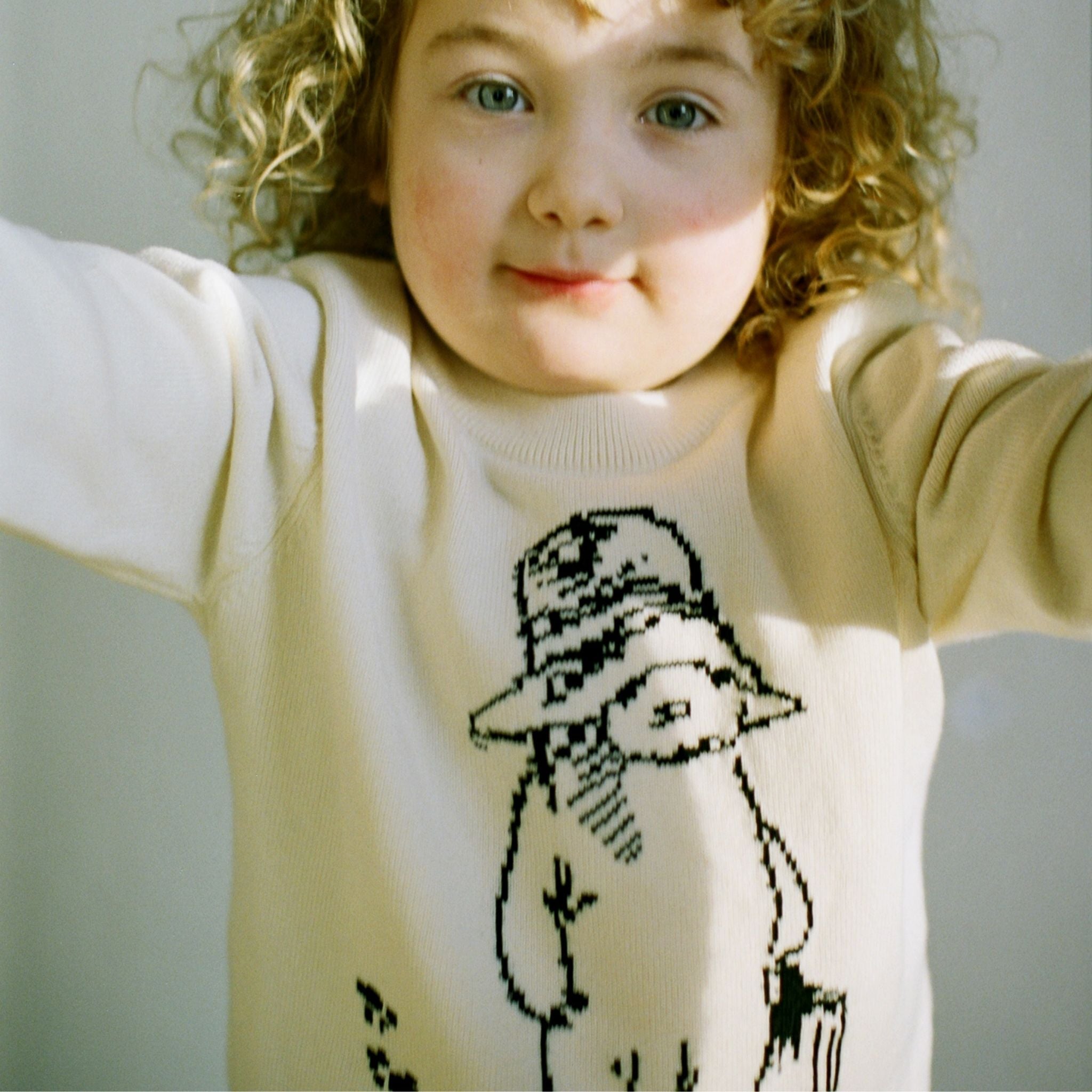 Close-up of child wearing the Sweater in ivory, showcasing the black knit illustration of Paddington Bear by Peggy Fortnum on soft cotton