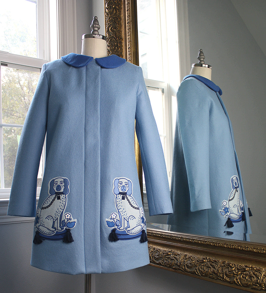 Ladies Aldrich and Madame De Bleu Coat in soft merino wool, featuring embroidered blue Staffordshire dog motifs with tassel details, reflected in a mirror