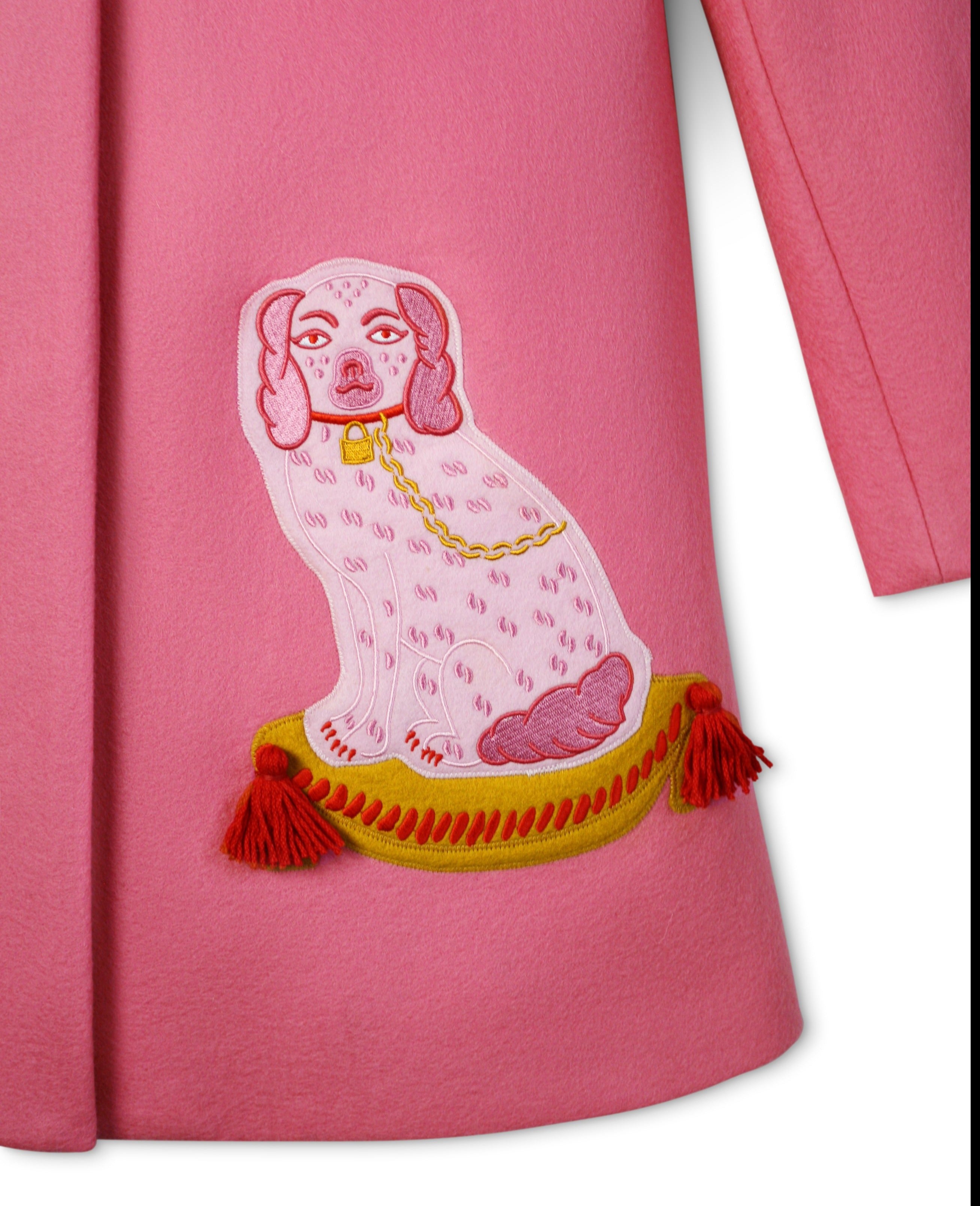Close-up of embroidered dog motif on pink wool coat, featuring a tufted pillow with tassel details