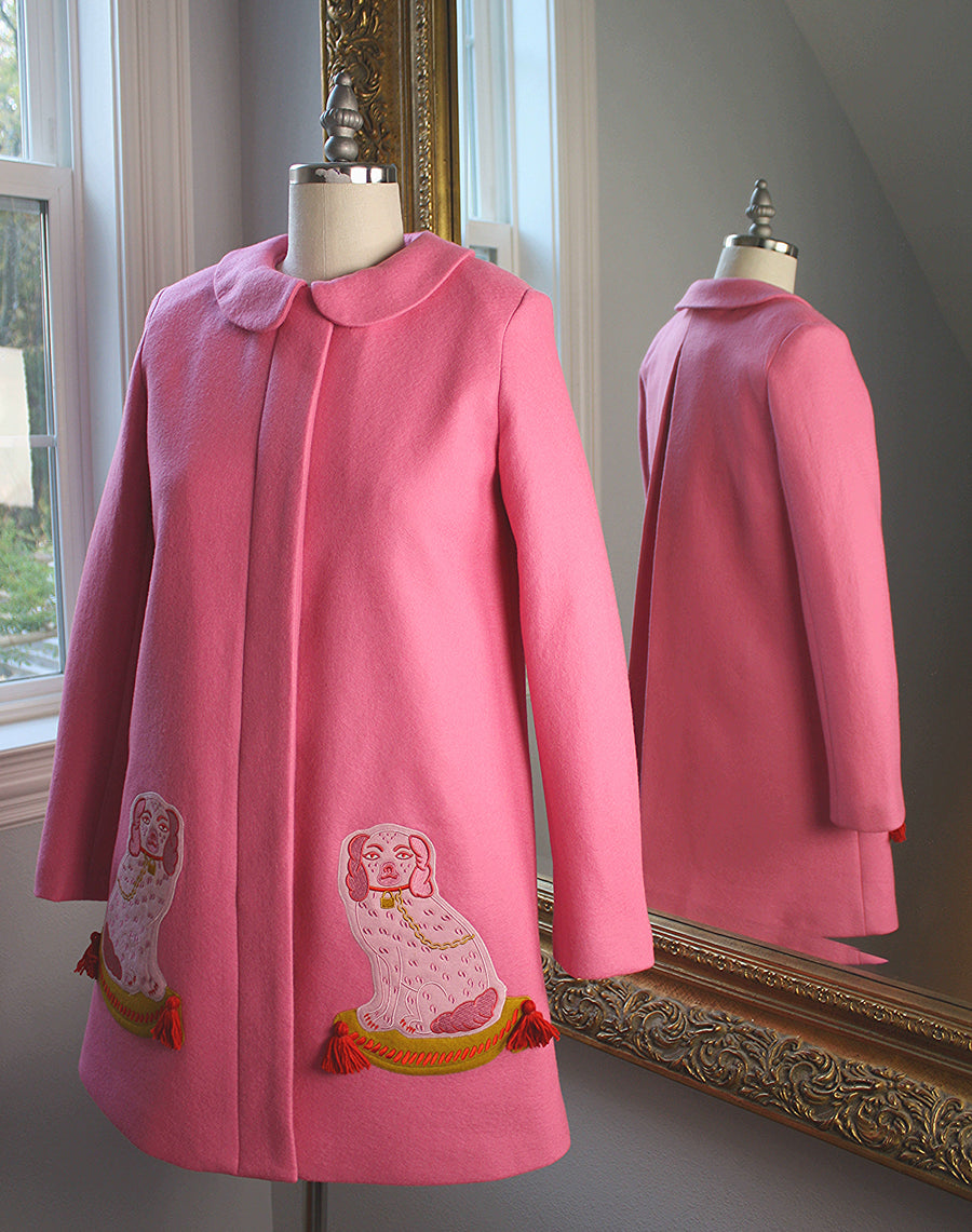 Pink wool A-line coat on form, featuring embroidered dog motifs, Peter Pan collar, and hidden placket, with back view reflected in mirror