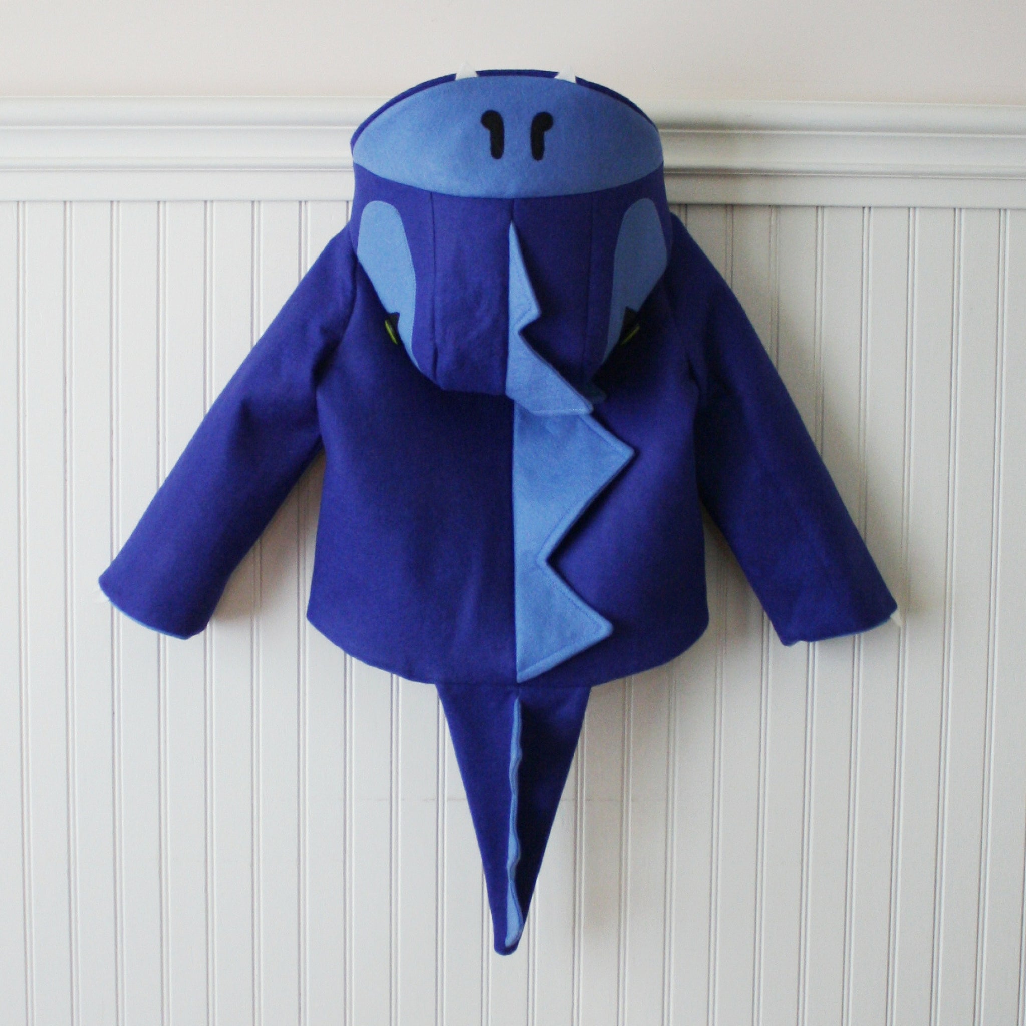 Back view of the Blithe Blue Dinosaur Coat by Little Goodall, featuring a ridged dinosaur hood, plush tail, and cozy wool blend fabric