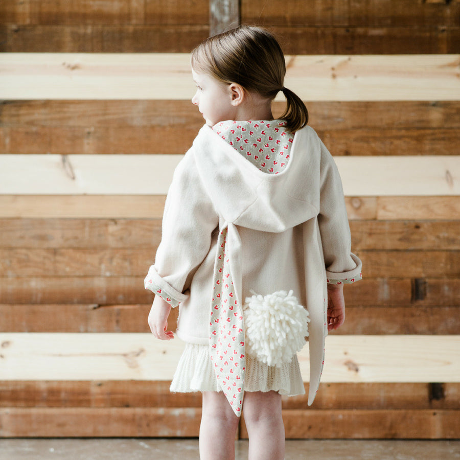 Child wearing a cream-colored bunny coat with a hood, long ears, and a fluffy tail, designed by Little Goodall.
