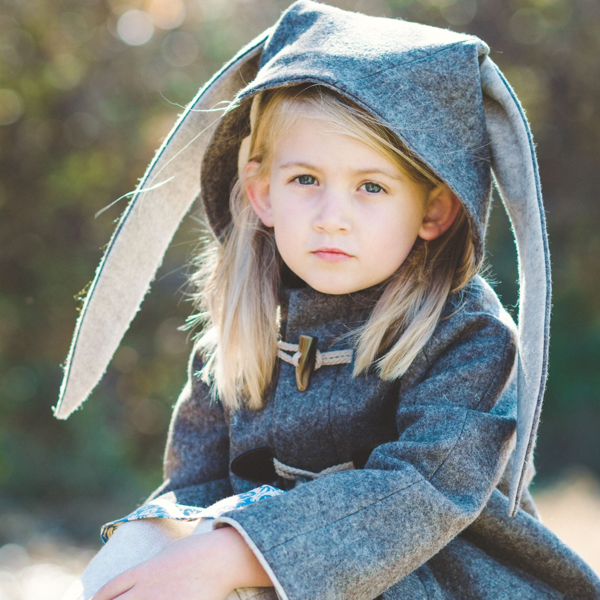 Close-up of a young girl outdoors wearing the Flopsy Bunny Coat, a handcrafted wool coat with bunny ears and toggle closures, 