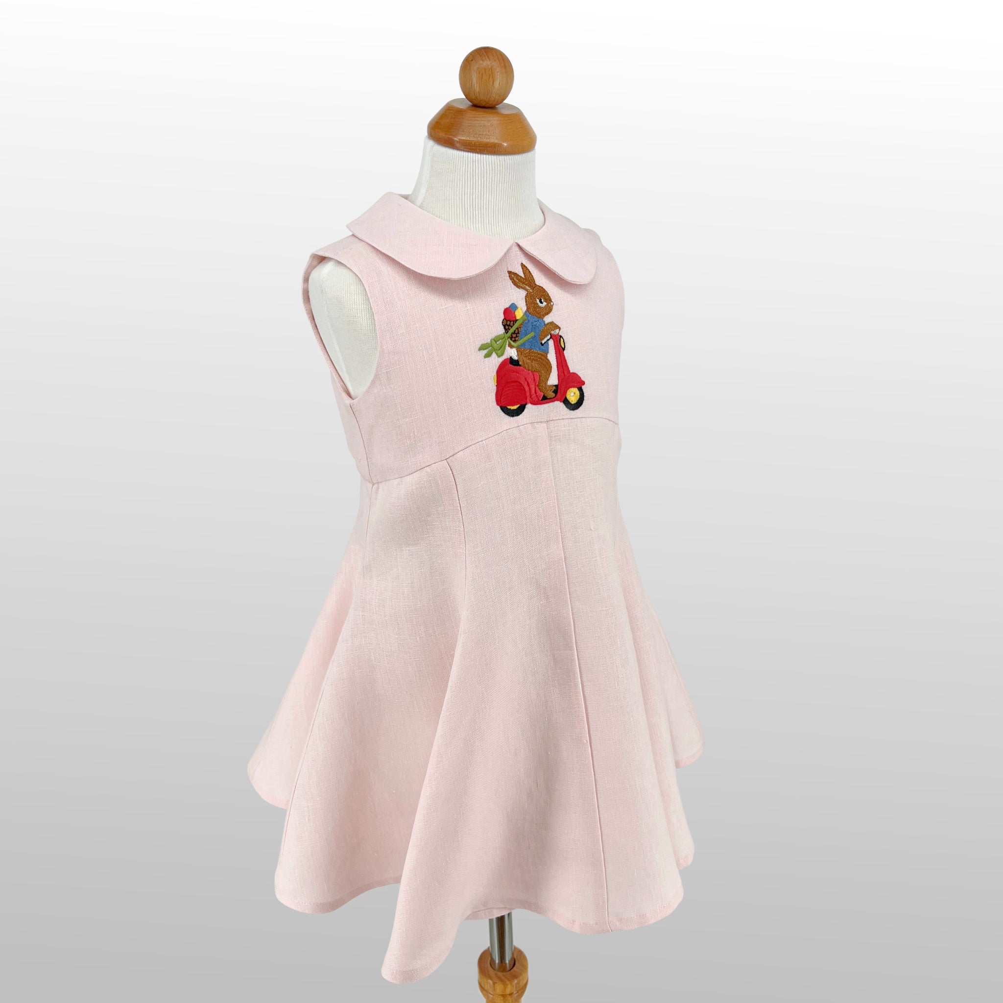 Side view of Linen Scooter Bunny Dress on mannequin, featuring embroidered bunny on scooter and flared skirt.