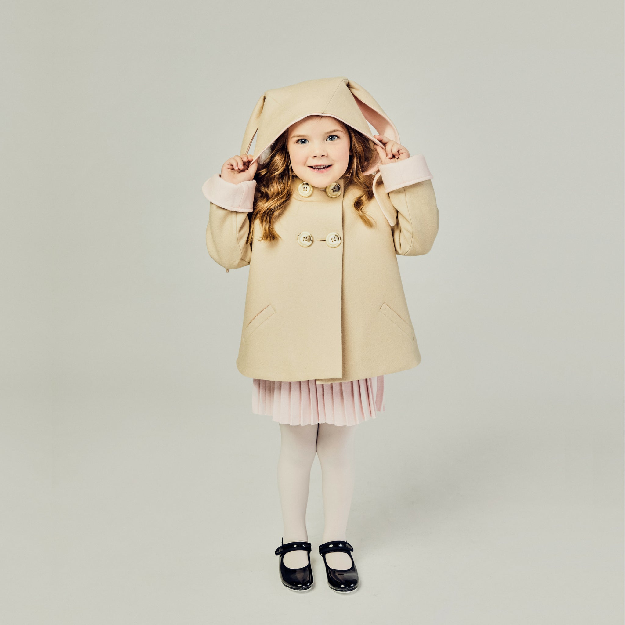 Child in the Luxe Bunny Coat in Sand & Pink, showing off satin cuffs and whimsical bunny ears on the hood.