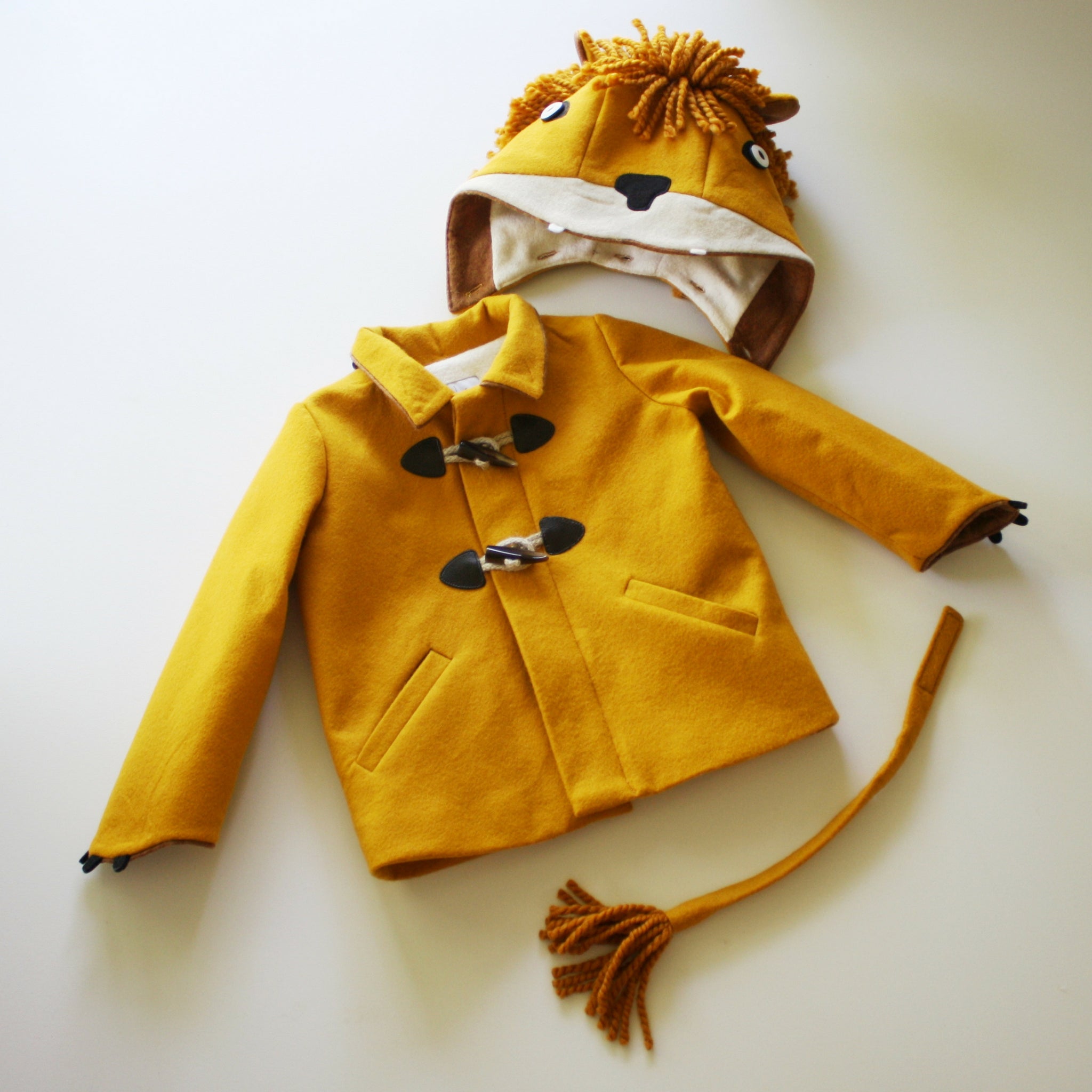 Flat lay of golden wool Luxe Lion Coat with detachable lion hood, soft mane, ears, rope toggle closures, claw-detailed cuffs, and matching tail.