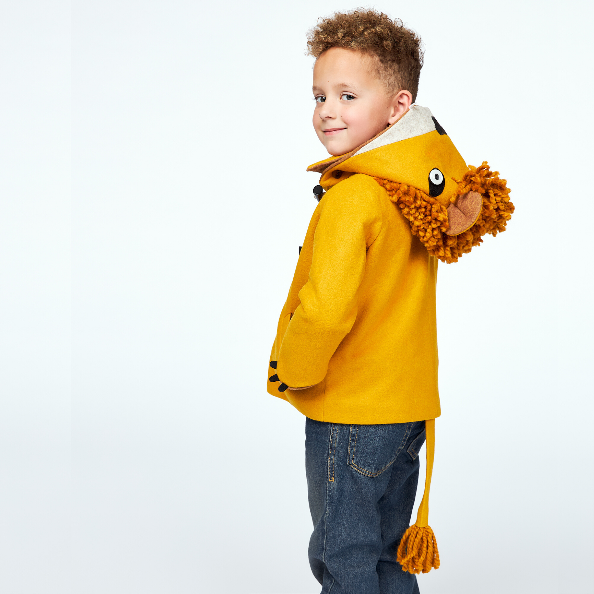 Boy wearing Little Goodall Luxe Lion Coat in gold wool, showing lion hood with mane, ears, and tail in a side view. Cozy and playful kids' jacket