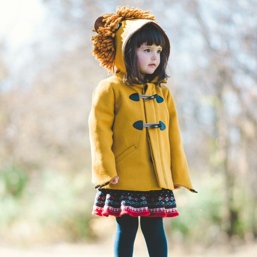 Child wearing Little Goodall Luxe Lion Coat in gold wool, standing outdoors with lion hood up. Cozy and stylish duffle jacket for fall and winter