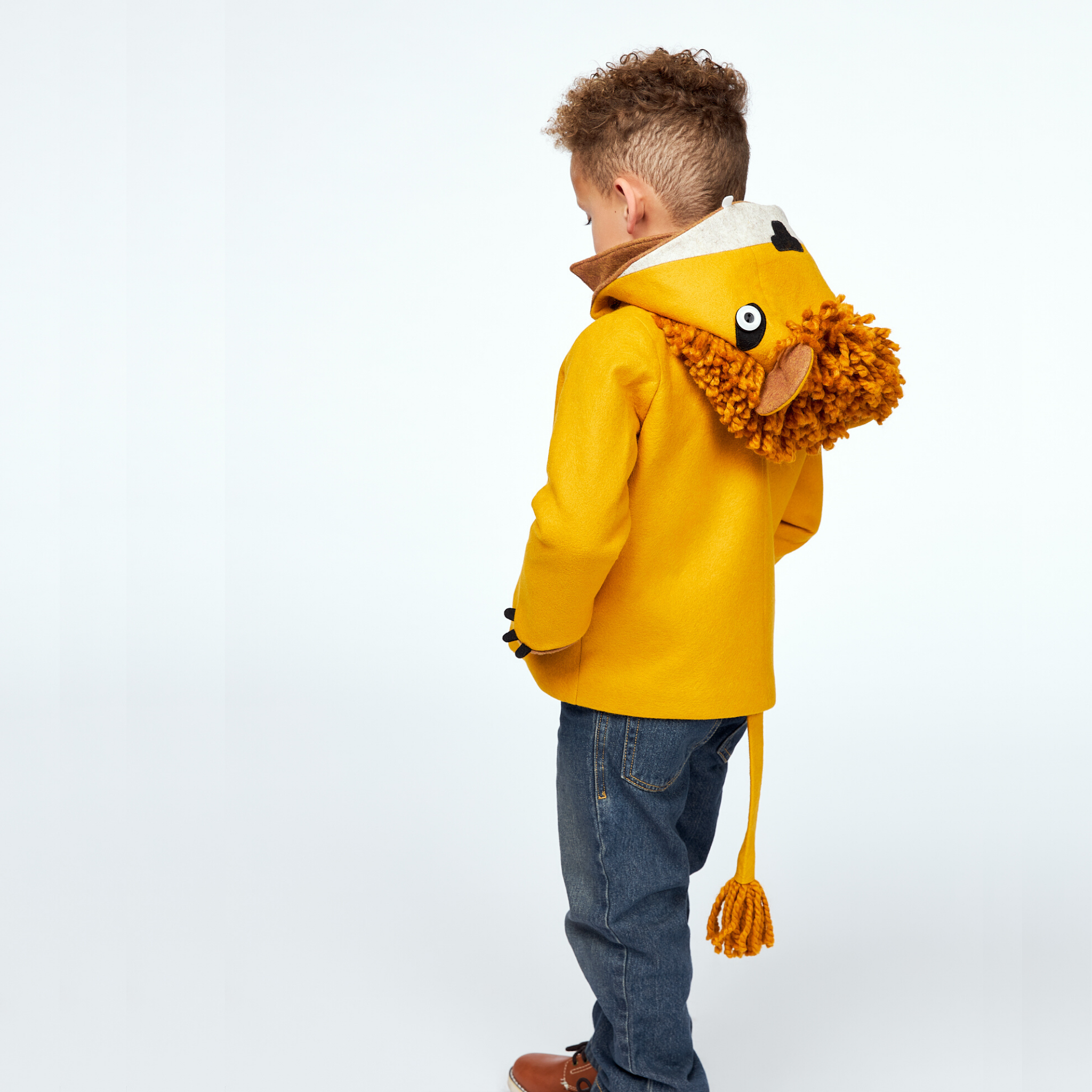 Boy wearing Little Goodall Luxe Lion Coat in gold wool, showing back view with lion hood, mane, and tail. Playful and cozy kids' jacket