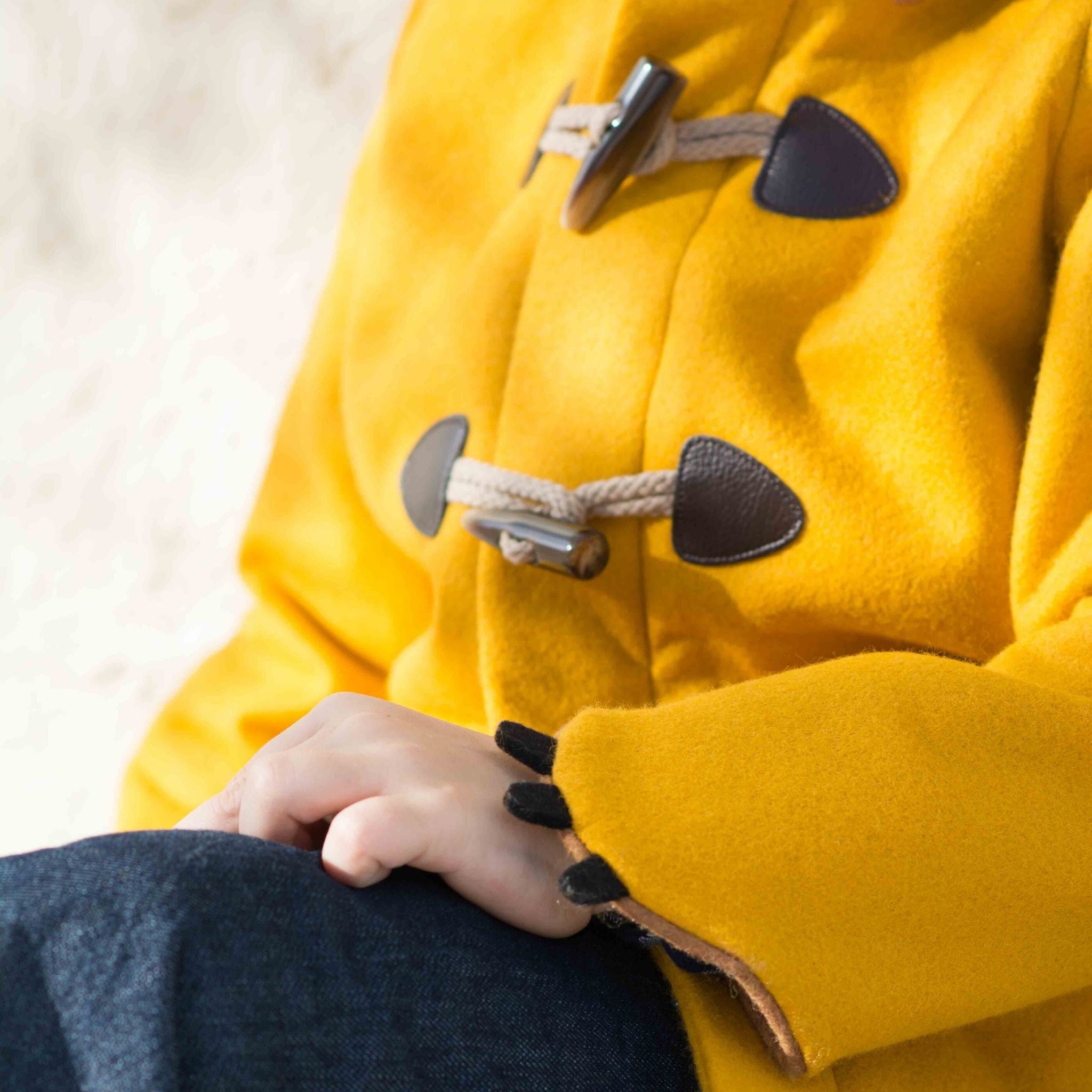 Close-up of Little Goodall Luxe Lion Coat featuring rope and toggle closures with faux leather details. Cuff styled with soft black claw accents