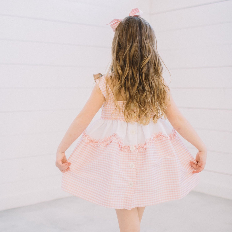 Back view of Little Goodall Pink Gingham Bunny Love Dress, featuring button details, ruffled trim, and gingham straps with bunny ear accents.