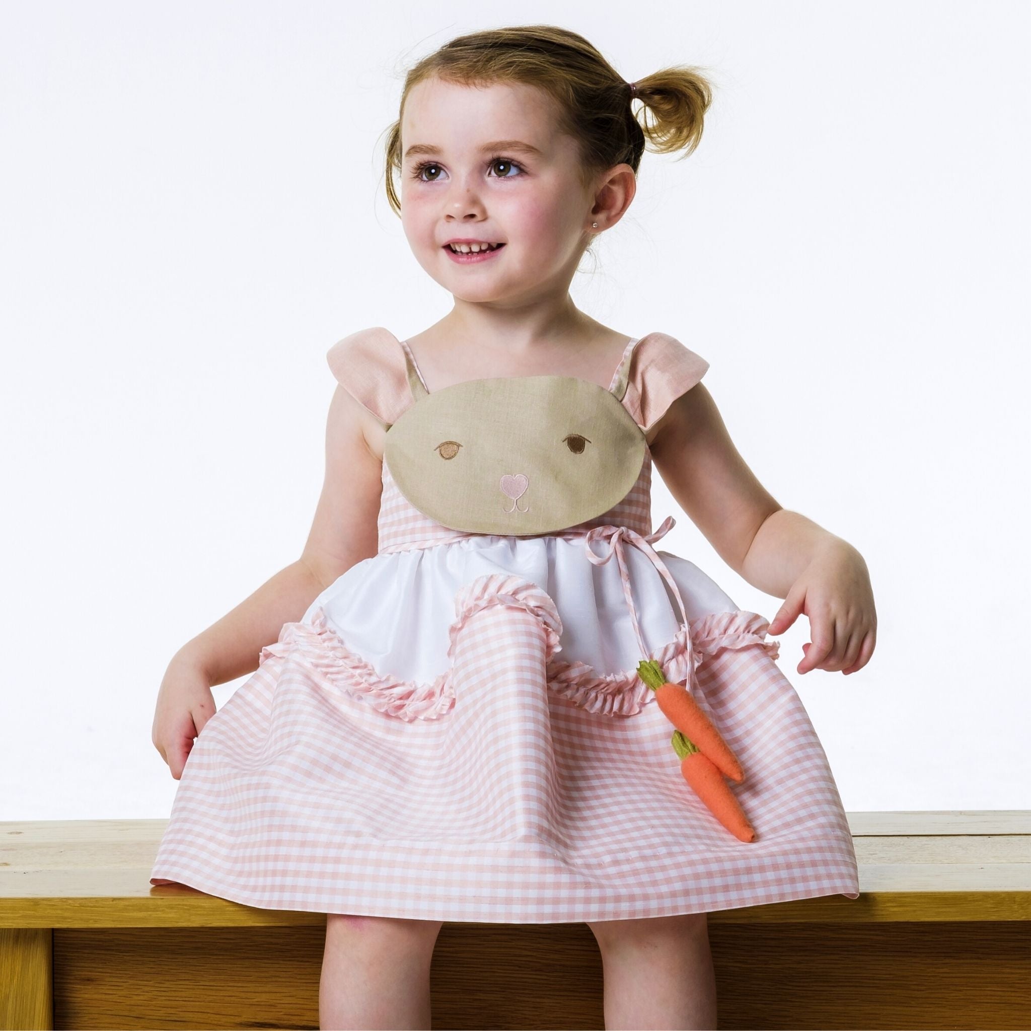 Toddler wearing Little Goodall Pink Gingham Bunny Love Dress with floppy ears, embroidered face, and carrot accents. Sweet and twirl-worthy.